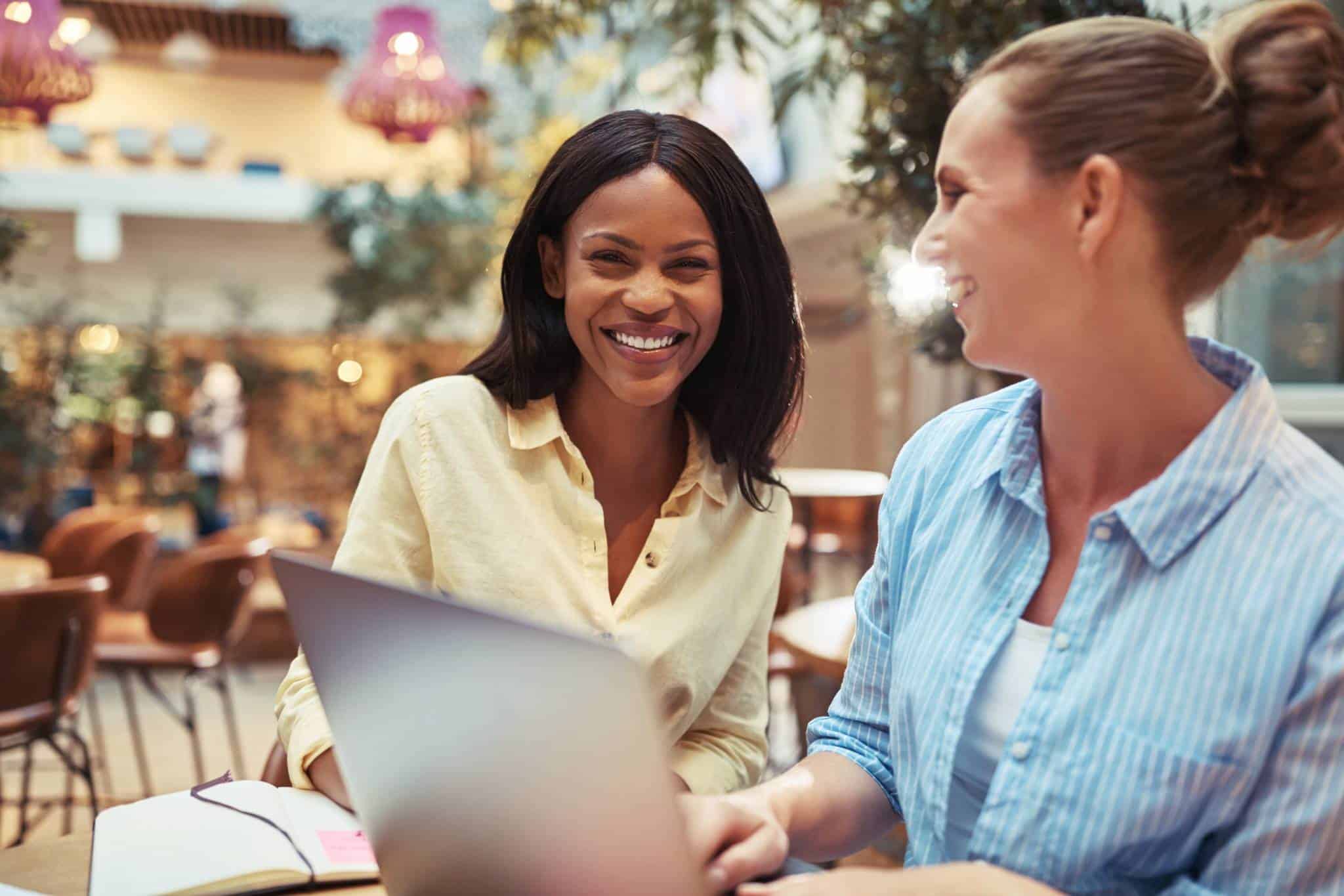 Dos empresarias sonrientes gestionando su restaurante desde un portátil, mostrando eficiencia y colaboración en un entorno acogedor